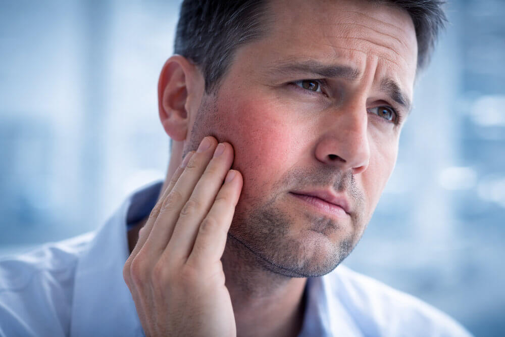 Мъж, който го боли лицето и се е хванал с ръка на мястото, където го боли